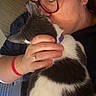 cat, black_and_white_cat, person, woman, glasses, kissing, cuddling, pet, affection, indoor, portrait, close_up, hand, ring, bracelet, laptop, keyboard, couch, furry, relaxed