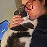 adult, black_and_white_cat, cat, cuddling, face, eyeglasses, hand, indoors, kissing, pet, pet_owner, portrait, sitting, soft_fur, tuxedo_cat, woman, affection, closeup, blue_screen, home