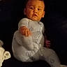 Karter is registered to the contest to win money with this photo: baby, child, infant, sitting, portrait, face, pajamas, white_clothing, couch, indoor, home, dark_background, serious_expression, looking_at_camera, hand, leg, toy, plush_toy, low_light, photography