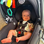 Ace is registered to the contest to win money with this photo: baby, car_seat, infant, child, seatbelt, toy, hanging_toy, black, fabric, safety, cute, smile, comfort, indoors, daylight, foot, hand, clothing, face, person