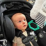 Ace is registered to the contest to win money with this photo: baby, car_seat, infant, child, seat_belt, toy, indoor, black, straps, curious, blue_eyes, clothing, safety, comfort, soft_toy, closeup, head_support, expression, looking_up, baby_care