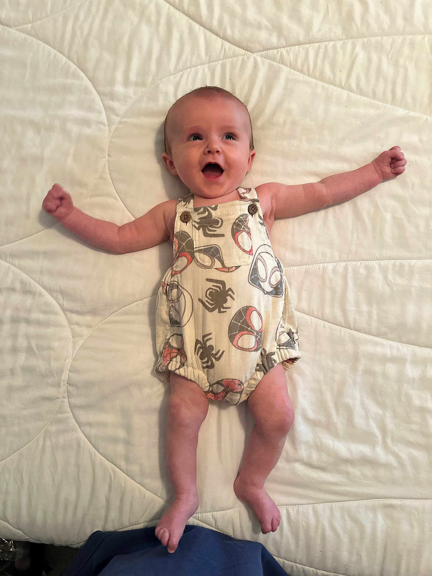 Ace is registered to the contest to win money with this photo: baby, infant, smiling, romper, clothing, arms_outstretched, lying_down, quilted_bedspread, happy, cute, infant_fashion, child, skin, foot, head, person, indoors, bed, expression, joyful
