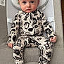 baby, infant, onesie, patterned_clothing, baby_seat, face, blue_eyes, serious_expression, indoor, wooden_floor, fabric, comfort, head_support, baby_clothes, child, person, cute, small_hands, footed_pajamas, sitting