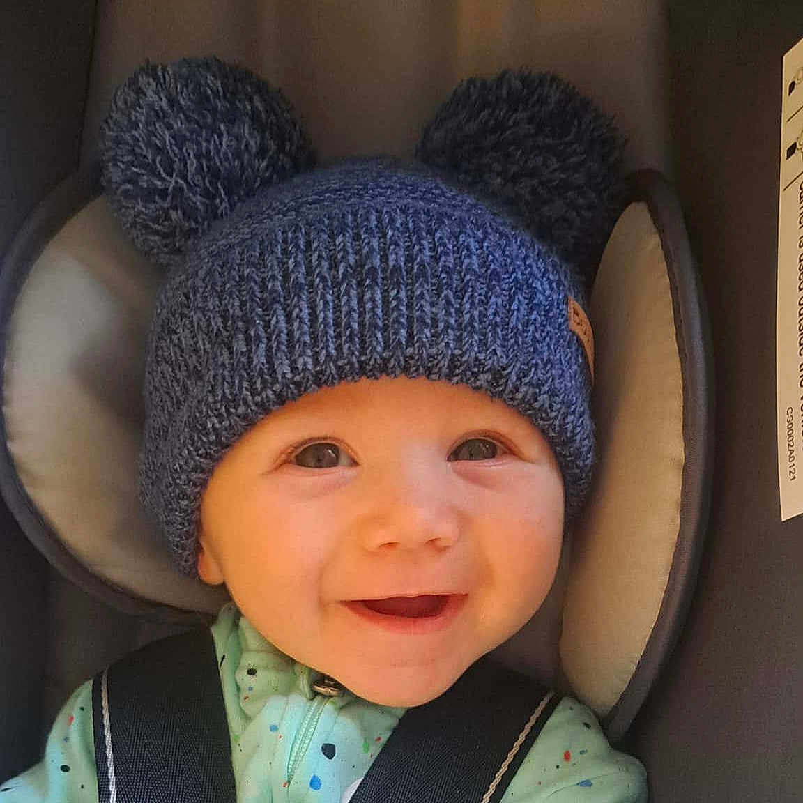 Noah is registered to the contest to win money with this photo: apparel, baby, car_seat, child, closeup, clothing, cute, face, happy, hat, headwear, indoors, infant, knit_hat, person, pom_poms, portrait, seatbelt, smiling, young_child