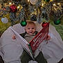 baby, child, book, reading, christmas_tree, christmas_ornaments, holiday, festive, smiling, indoor, cozy, blanket, green_clothing, red, white, decorations, holiday_lighting, cute, happy, infant