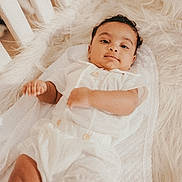 Ezra is registered to the contest to win money with this photo: baby, infant, crib, white_clothing, blanket, fluffy, soft_texture, lying_down, cute, child, portrait, indoors, sleepwear, peaceful, resting, young_child, skin, face, hand, cozy