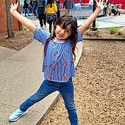 Graciela is registered to the contest to win money with this photo: child, girl, smiling, posing, blue_top, jeans, sneakers, outdoor, playground, wood_chips, sidewalk, trees, people, park, daylight, casual_clothing, happy, fun, nature, recreation