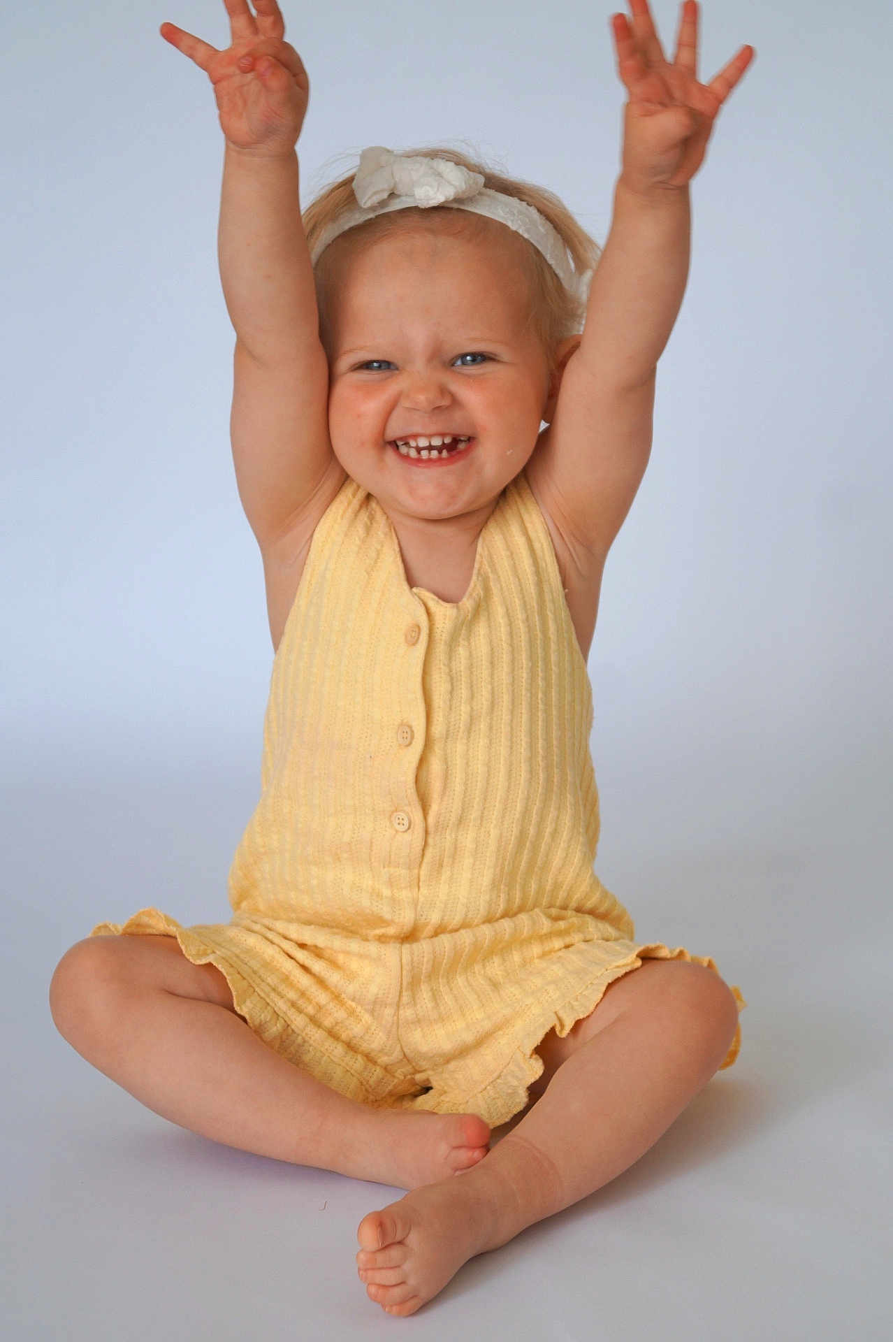 Lina a rejoint le concours — aidez-le/la à gagner de superbes lots ! toddler, child, smiling, yellow_clothing, headband, barefoot, sitting, raising_arms, happy, studio, portrait, cute, baby, indoor, light_background, short_hair, buttoned_outfit, skin, feet, hands