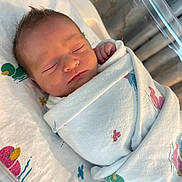 Malakai is registered to the contest to win money with this photo: newborn, baby, sleeping, wrapped, blanket, hospital, bassinet, duck_pattern, infant, cute, peaceful, child, swaddled, face, head, skin, hair, indoors, resting, portrait