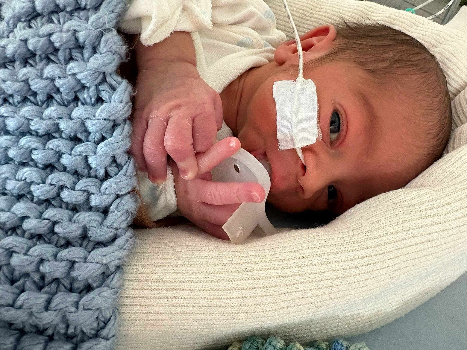 Elio a rejoint le concours — aidez-le/la à gagner de superbes lots ! newborn, baby, infant, blanket, knitted, pacifier, feeding_tube, medical, hospital, cozy, wrapped, cute, small_hand, face, eyes, resting, laying, soft, warm, person