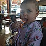 toddler, child, high_chair, indoor, restaurant, window, sunlight, packet, food, jacket, floral_pattern, seat, table, floor, curious, person, face, hand, daylight, casual