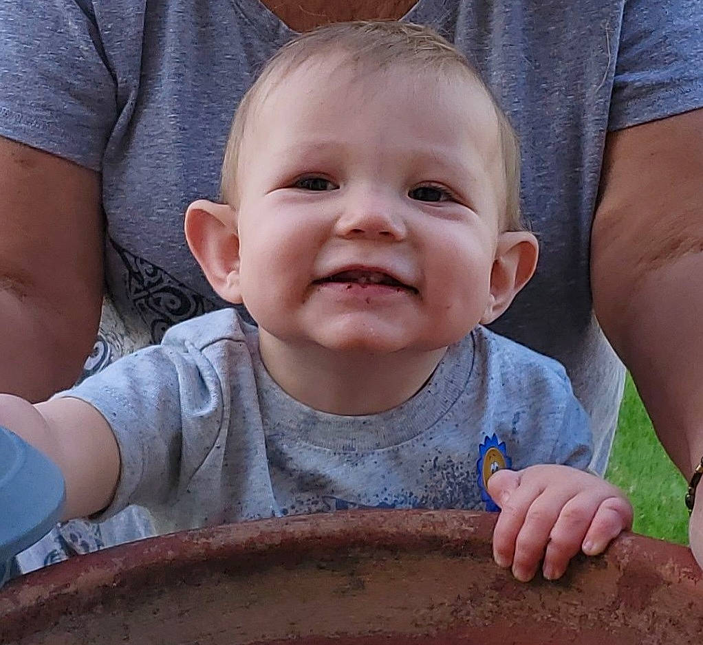 Thorsten is registered to the contest to win money with this photo: baby, baby_toddler_clothing, cheek, child, clothing, eye, facial_expression, finger, gesture, grass, happy, joy, mouth, person, product, sitting, skin, sleeve, smile, t_shirt