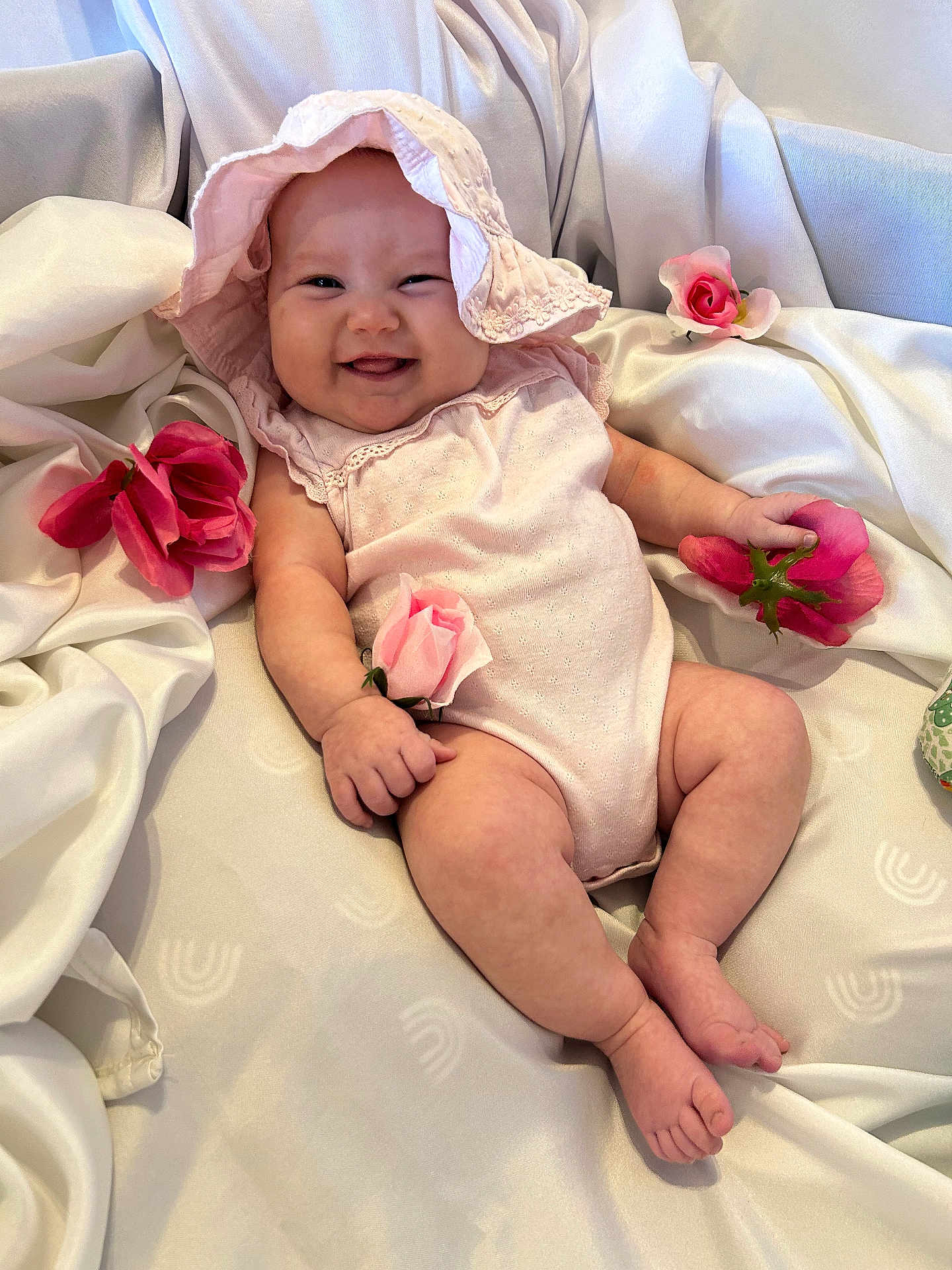Hazel joined the competition — help win amazing prizes! baby, smiling, pink_hat, pink_outfit, roses, flower, white_fabric, cute, infant, portrait, chubby_arms, chubby_legs, happy, indoors, soft_lighting, baby_girl, laying_down, closeup, skin, hand_holding_flower