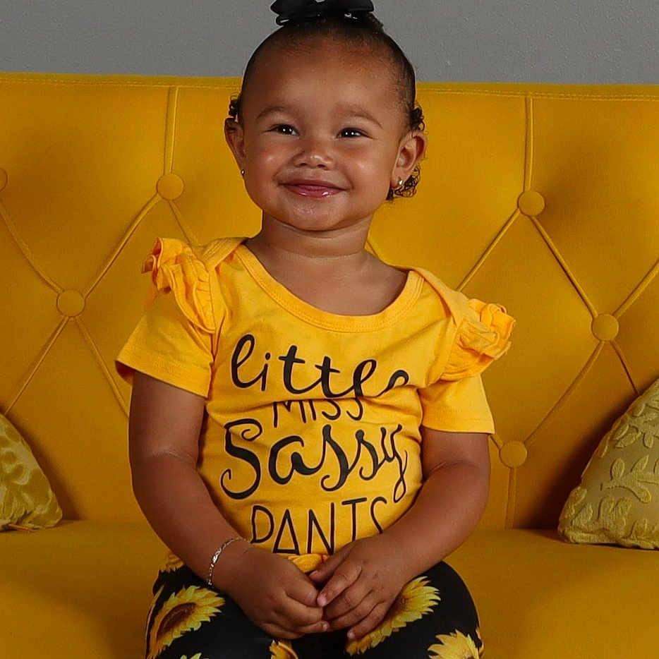 K'Leerose joined the competition — help win amazing prizes! black_bow, bracelet, bright_colors, casual, child, cute, fashion, hair_accessory, happy, indoor, leggings, person, portrait, shoes, sitting, smiling, sunflower_pattern, toddler, yellow_clothing, yellow_couch
