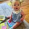 Madelyn is registered to the contest to win money with this photo: baby, child, indoor, carpet, books, blue_gingham, white_collar, flooring, wooden_floor, sitting, curious, tousled_hair, sock, toy, reading, playroom, cute, portrait, person, infant