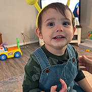 Jax is registered to the contest to win money with this photo: toddler, child, indoor, headband, yellow, bunny_ears, glasses, denim_overalls, camouflage_shirt, smiling, toy, floor, carpet, television, furniture, person, happy, cute, playful, home