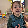 toddler, child, indoor, headband, yellow, bunny_ears, glasses, denim_overalls, camouflage_shirt, smiling, toy, floor, carpet, television, furniture, person, happy, cute, playful, home
