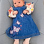 baby, infant, denim_dress, butterfly, colorful_clothing, socks, chair, cushion, indoor, person, portrait, cute, small_hands, soft_furniture, curious_expression, seated, child, newborn, fashion, cozy