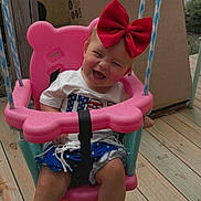 Paityn is registered to the contest to win money with this photo: toddler, child, swing, pink_swing, red_bow, smiling, happy, outdoor, wooden_deck, cardboard_box, summer_clothes, barefoot, playtime, fun, rope, seat, person, baby, cute, cheerful