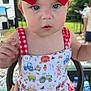baby, background_people, blue_eyes, child, closeup, curious, daylight, farm_print, greenery, hand, nature, outdoor, person, red_bow, romper, sitting, summer_clothing, sunlight, vehicle, white_skin