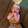 Noah is registered to the contest to win money with this photo: baby, child, hat, bucket_hat, smiling, happy, sitting, couch, cushion, indoor, clothing, infant, hands, mouth, face, person, textile, floor, carpet, relaxed