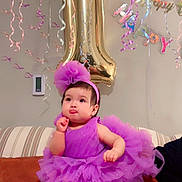 Aylin joined the competition — help win amazing prizes! baby, balloon, birthday, celebration, child, couch, cute, decorations, festive, footwear, headband, indoor, number_one, party, person, purple_dress, ribbon, smiling, streamers, tutu