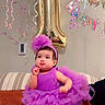 baby, balloon, birthday, celebration, child, couch, cute, decorations, festive, footwear, headband, indoor, number_one, party, person, purple_dress, ribbon, smiling, streamers, tutu