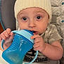 baby, blue_sippy_cup, child, closeup, clothing, curious, cute, expression, face, feeding, hands, high_chair, indoor, infant, knit_hat, person, plastic_cup, portrait, seated, table
