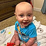 baby, child, smiling, blue_shirt, toy, blanket, indoor, carpet, wooden_furniture, happy, sitting, cute, infant, playtime, person, face, young_child, toddler, colorful, room