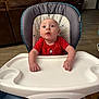 baby, child, couch, curious, door, expression, flooring, food, furniture, high_chair, home, indoor, infant, living_room, person, plastic_tray, red_shirt, seat, window, wood_floor