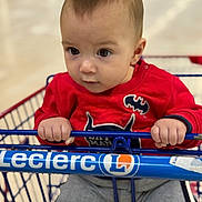 Leví a rejoint le concours — aidez-le/la à gagner de superbes lots ! baby, child, shopping_cart, red_sweater, batman_logo, gray_pants, indoor, hands, face, eyes, infant, clothing, person, portrait, grip, cute, curious, young_child, retail, store