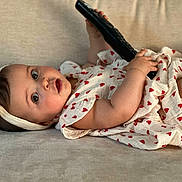 Agathe participe au concours pour gagner de l'argent avec cette photo : baby, child, infant, couch, remote_control, headband, heart_pattern, dress, soft_furniture, curious, lying_down, indoors, cute, adorable, skin, hand, face, eyes, expression, comfort