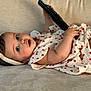 baby, child, infant, couch, remote_control, headband, heart_pattern, dress, soft_furniture, curious, lying_down, indoors, cute, adorable, skin, hand, face, eyes, expression, comfort