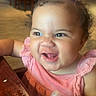 toddler, child, pink_dress, pink_bow, bottle, funny_face, table, restaurant, wooden_table, curly_hair, happy, indoor, person, baby, cute, smile, drinking, seat, furniture, expression