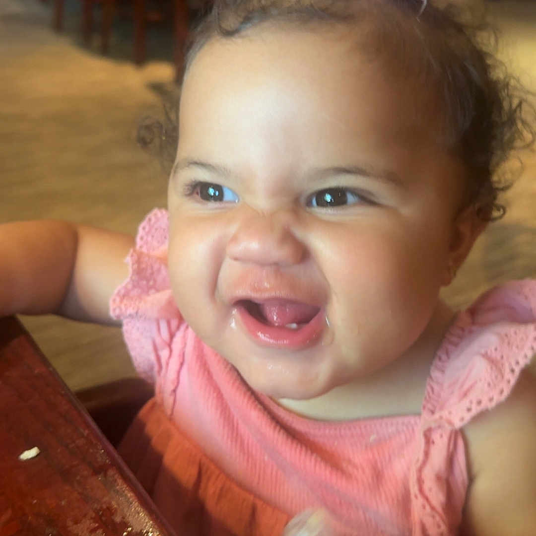 Addi-Lee joined the competition — help win amazing prizes! baby, bottle, child, curly_hair, cute, drinking, expression, funny_face, furniture, happy, indoor, person, pink_bow, pink_dress, restaurant, seat, smile, table, toddler, wooden_table