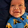 baby, infant, smile, face, onesie, clothing, blue, yellow, black, construction_vehicle_pattern, joy, expression, portrait, child, cute, happy, closeup, person, background, fabric