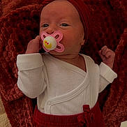 Ambre participe au concours pour gagner de l'argent avec cette photo : baby, infant, pacifier, red_clothing, white_clothing, blanket, newborn, face, headwear, lying_down, cute, small_hands, cozy, indoors, soft_texture, closeup, portrait, child, expression, resting