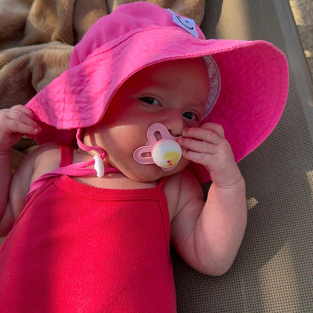 Ambre participe au concours pour gagner de l'argent avec cette photo : baby, blanket, child, cute, daylight, face, hand, infant, lounge_chair, outdoor, pacifier, pink_hat, portrait, red_clothing, relaxing, shade, skin, summer, sunlight, water_bottle