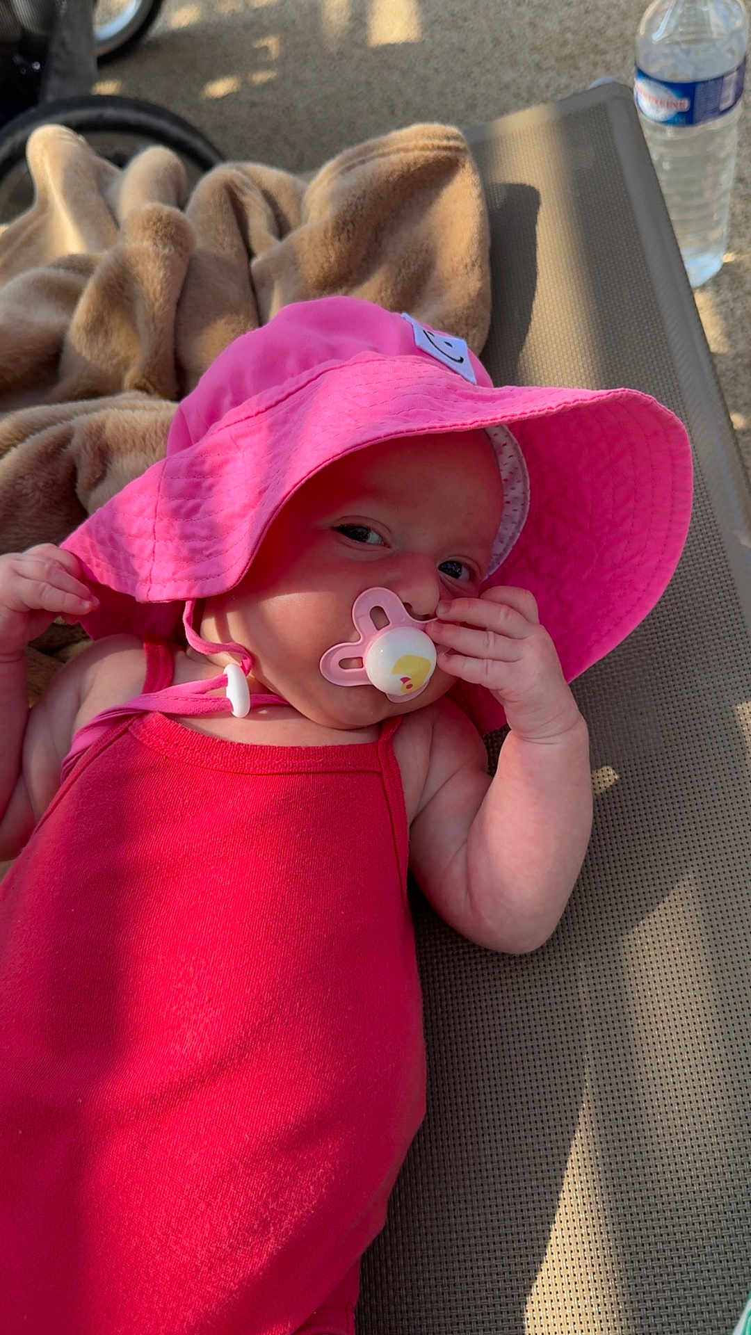 Ambre participe au concours pour gagner de l'argent avec cette photo : baby, infant, pink_hat, pacifier, red_clothing, blanket, lounge_chair, water_bottle, outdoor, sunlight, relaxing, child, cute, skin, hand, face, portrait, summer, shade, daylight
