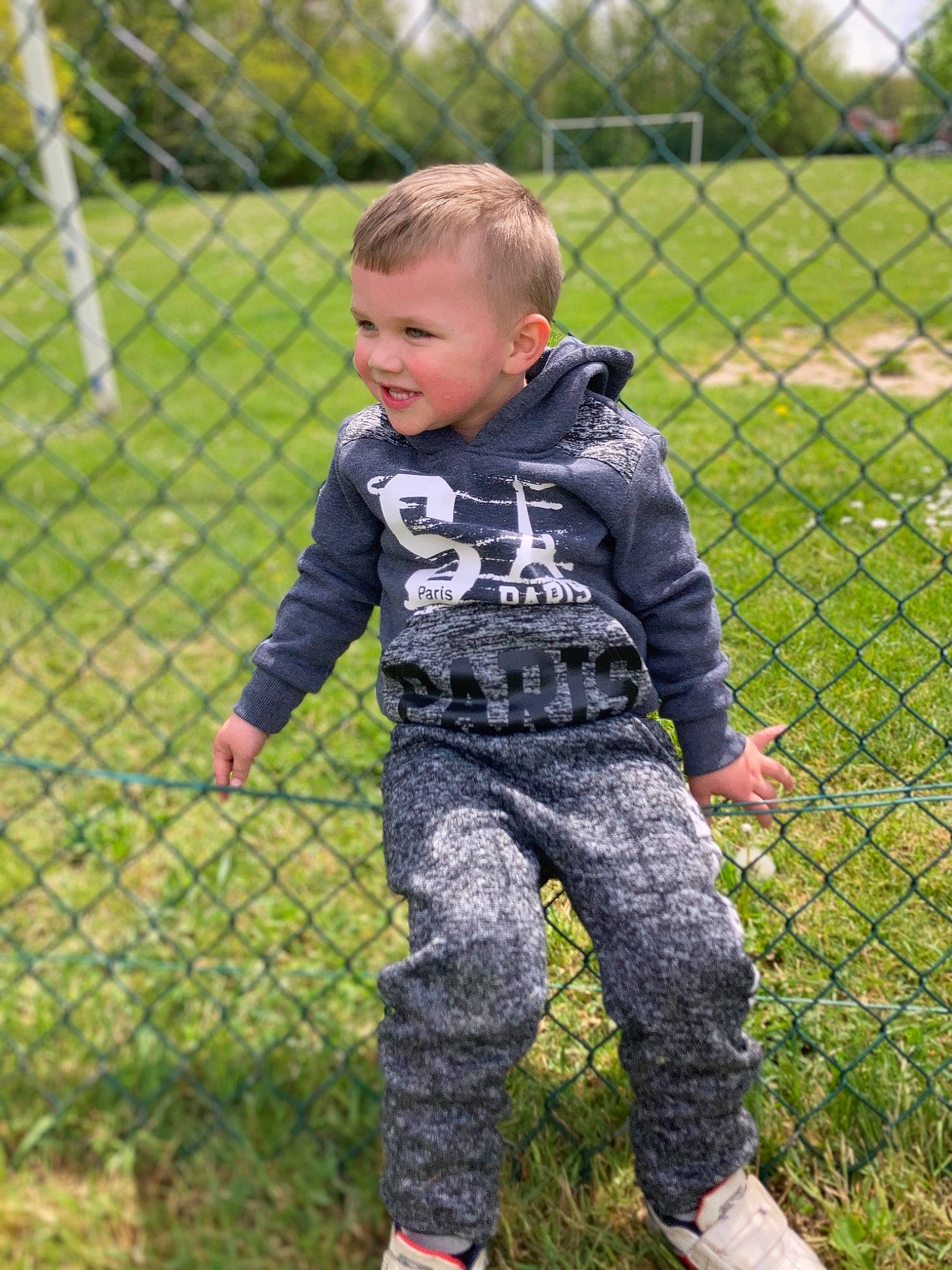 Mayron participe au concours pour gagner de l'argent avec cette photo : baby_toddler_clothing, chain_link_fencing, fence, grass, jacket, joy, leisure, mesh, net, pattern, people_in_nature, person, plant, player, recreation, sleeve, smile, soil, t_shirt, toddler