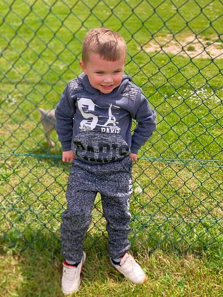 Mayron a rejoint le concours — aidez-le/la à gagner de superbes lots ! baby_toddler_clothing, chain_link_fencing, face, fence, fun, grass, grass_family, grassland, joy, lawn, leaf, mesh, net, pattern, people_in_nature, person, player, sleeve, smile, t_shirt