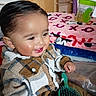 toddler, child, smiling, plaid_shirt, hairbrush, indoors, blanket, dresser, furniture, happy, person, clothing, face, hair, buttoned_shirt, seated, room, wood, toy, colorful