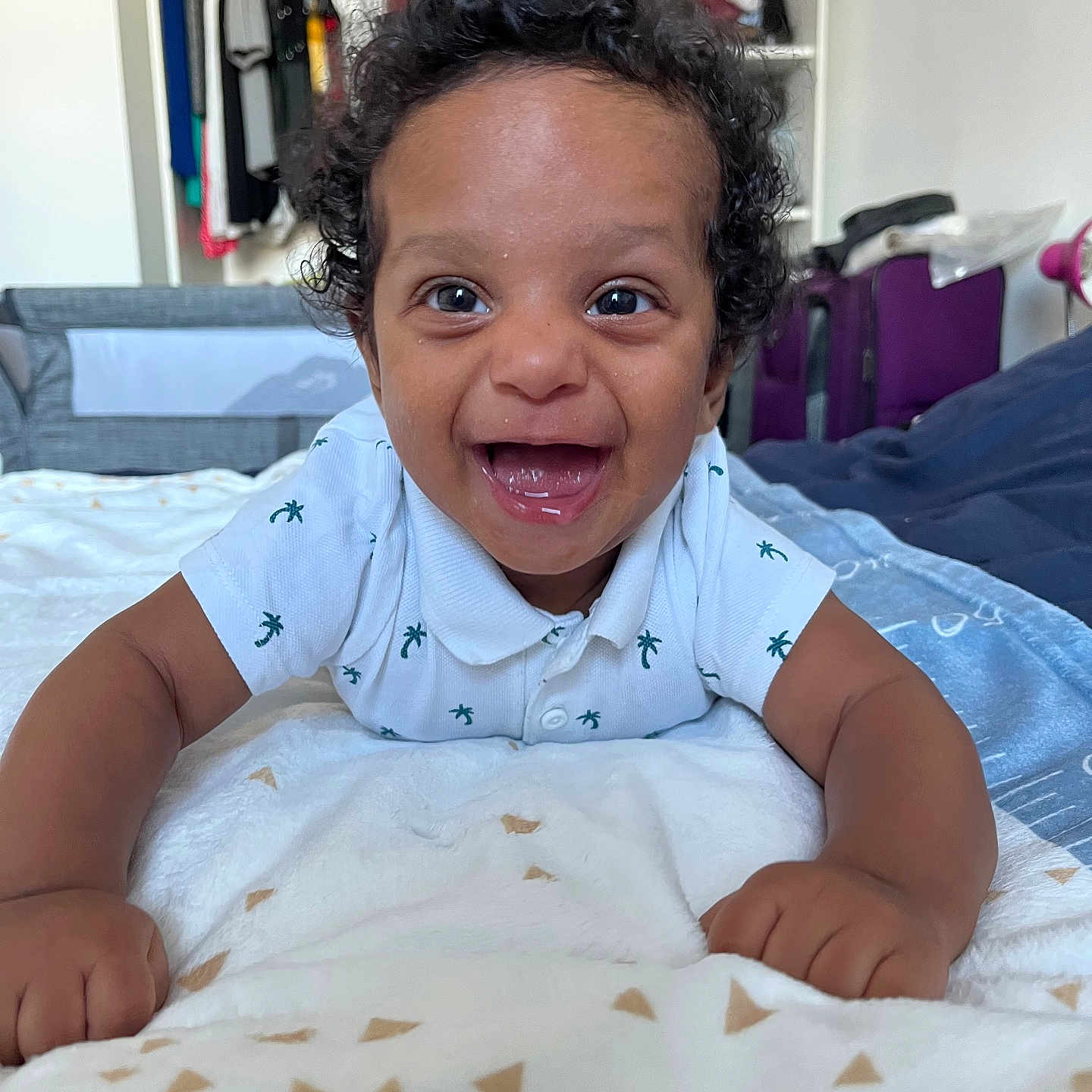 Elyonn a rejoint le concours — aidez-le/la à gagner de superbes lots ! baby, bedroom, blanket, child, clothing, curly_hair, cute, face, furniture, happy, home, indoor, infant, lying_down, person, playful, portrait, smiling, toddler, white_shirt