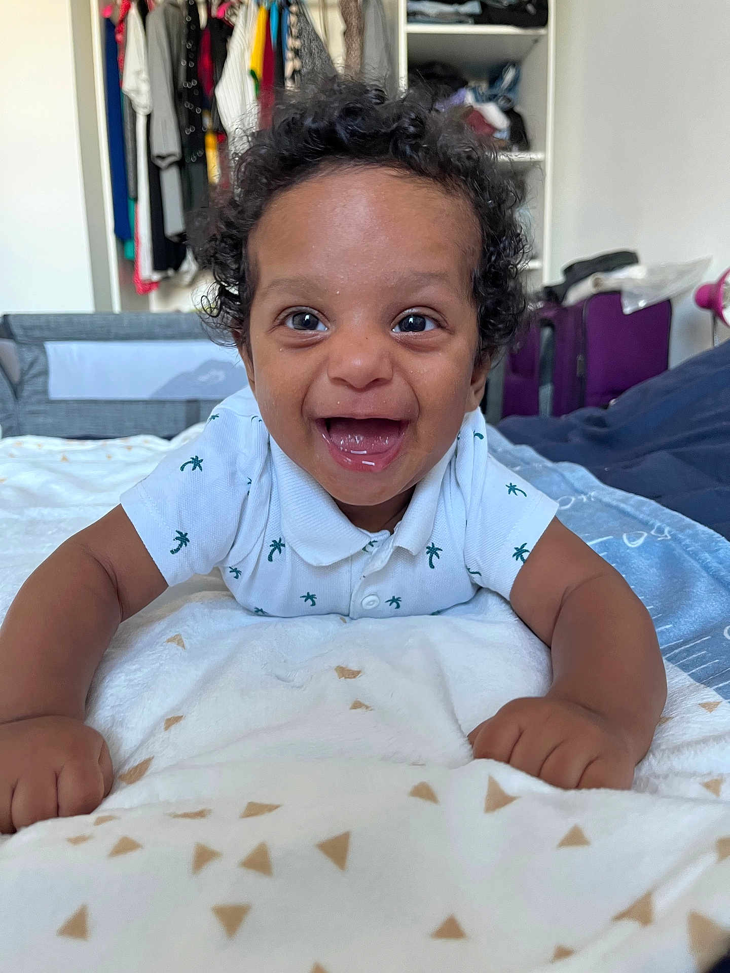 Elyonn a rejoint le concours — aidez-le/la à gagner de superbes lots ! baby, bedroom, blanket, child, clothing, curly_hair, cute, face, furniture, happy, home, indoor, infant, lying_down, person, playful, portrait, smiling, toddler, white_shirt