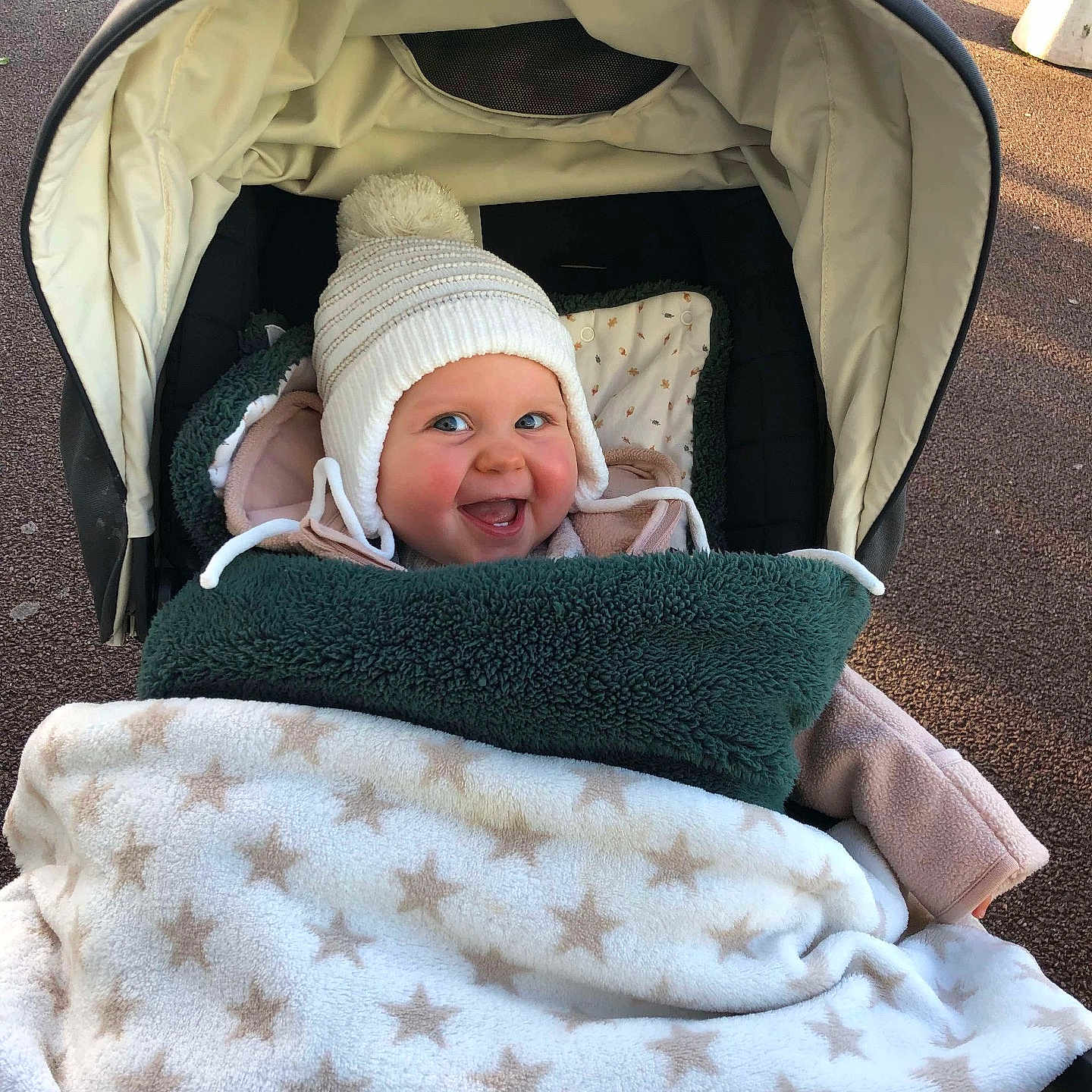 Jade a rejoint le concours — aidez-le/la à gagner de superbes lots ! baby, blanket, child, cold_weather, cozy, cute, face, happy, hat, headwear, infant, outdoor, pattern, person, pom_pom, smile, stroller, textile, transportation, warm_clothing