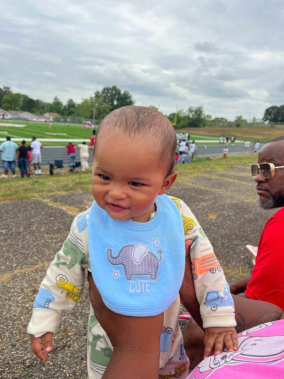 Amir joined the competition — help win amazing prizes! baby, child, bib, elephant, cute, hand, adult, sports_field, people, crowd, cloudy_sky, outdoor, spectator, glasses, red_shirt, grass, track, pavement, smile, portrait