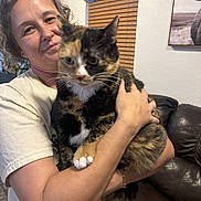 Sophie joined the competition — help win amazing prizes! person, cat, calico_cat, indoor, smiling, holding, pet, window, blinds, couch, furniture, wall, portrait, happy, animal, domestic_animal, home, cozy, curly_hair, arm