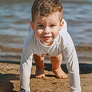 Diego a rejoint le concours — aidez-le/la à gagner de superbes lots ! child, sand, water, beach, crawling, smiling, sunlight, long_sleeve_shirt, barefoot, outdoor, playful, young_child, close_up, nature, daylight, happy, casual_clothing, curly_hair, face, skin