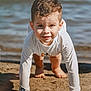 child, sand, water, beach, crawling, smiling, sunlight, long_sleeve_shirt, barefoot, outdoor, playful, young_child, close_up, nature, daylight, happy, casual_clothing, curly_hair, face, skin