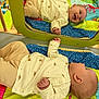 baby, infant, mirror, reflection, play_mat, colorful, smiling, lying_down, clothing, turtle_print, wooden_frame, green_frame, happy, child, indoor, soft_toys, bright_colors, cute, casual, peaceful